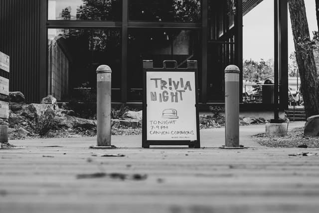 A black and white image showing a sign promoting a trivia night.