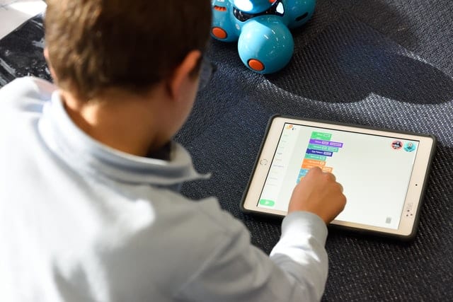 Ein Schüler programmiert mit einer visuellen Programmiersprache einen Roboter auf seinem Schul-Tablet