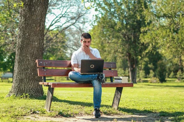 Ein Mann sitzt auf einer Parkbank mit Laptop auf dem Schoß